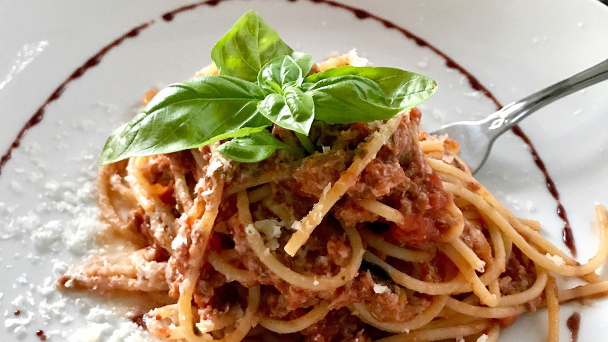 Spaghetti and meat sauce wrapped around a fork with leafy adornment